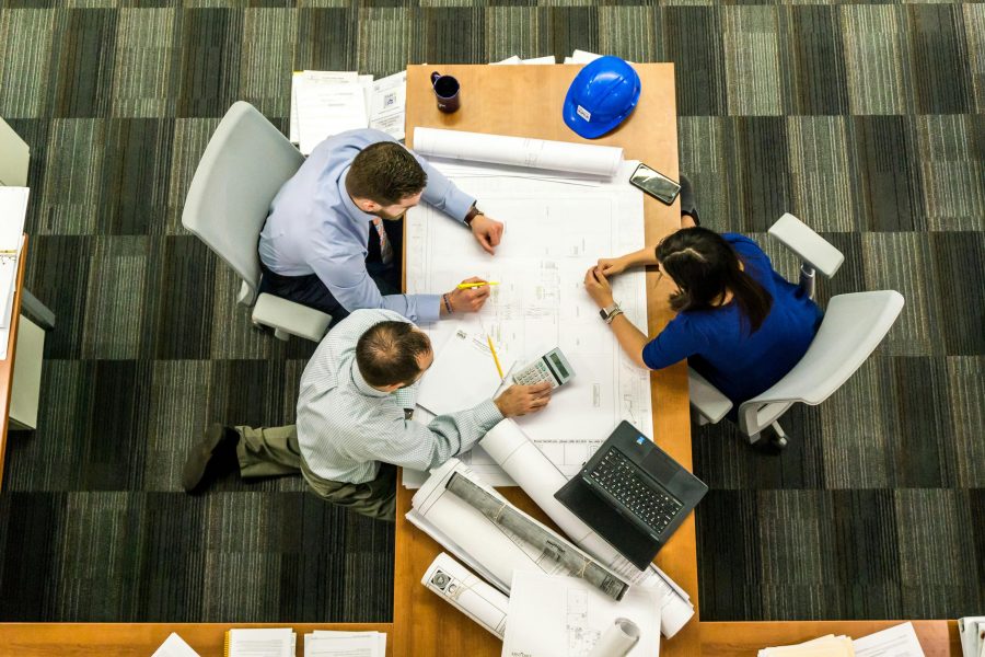 overhead view of 3 people planning, calculating and discussing at a meeting table